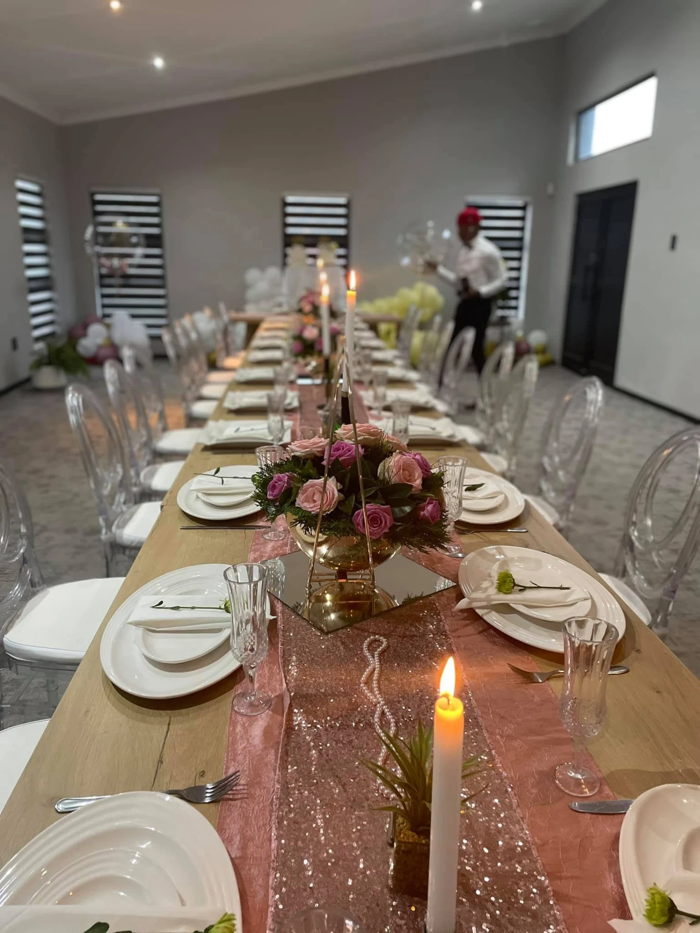 Long banquet table styled with candles, roses and gold accents for a celebration